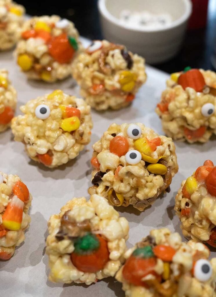 Completed popcorn balls are on a baking sheet, among some dishes and containers.