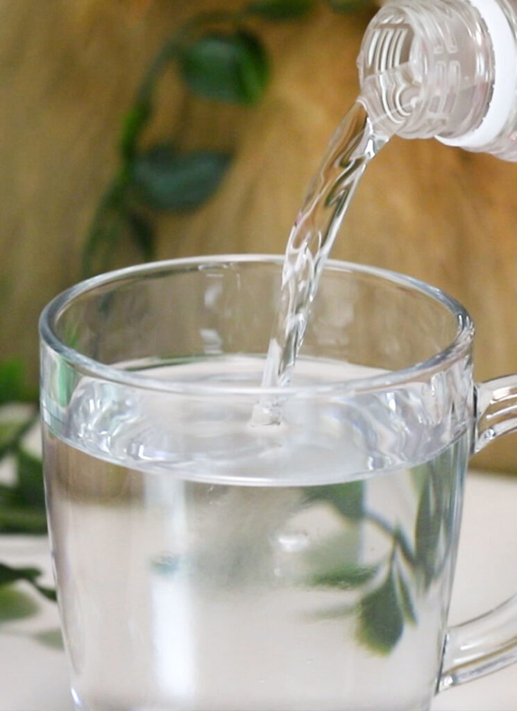 Vinegar is being poured into a glass of water.