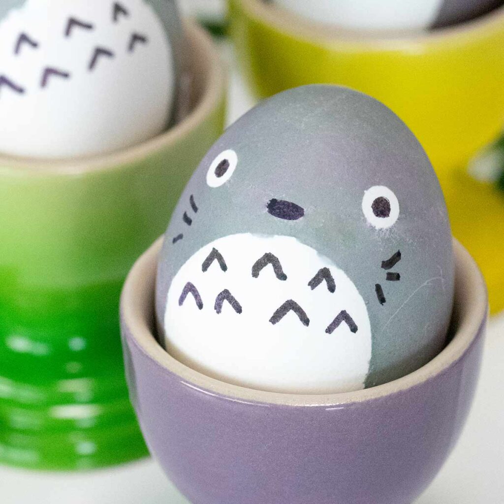 An Easter egg decorated to look like Totoro sits in a purple egg cup.