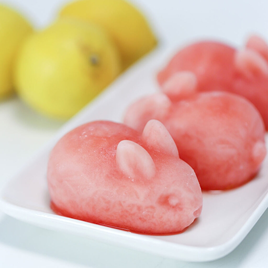Three rabbit-shaped pink lemonade drink bombs sit on a white plate. Lemons are in the background.