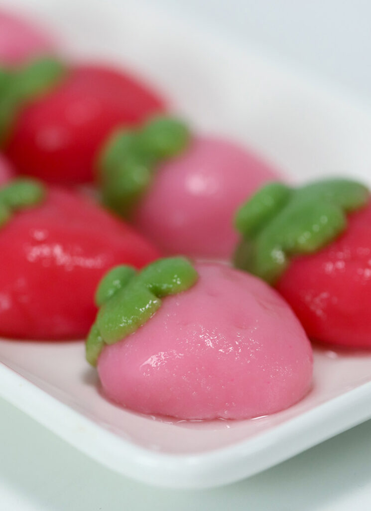 Pink and red strawberry-shaped mochi are on a white rectangular plate.