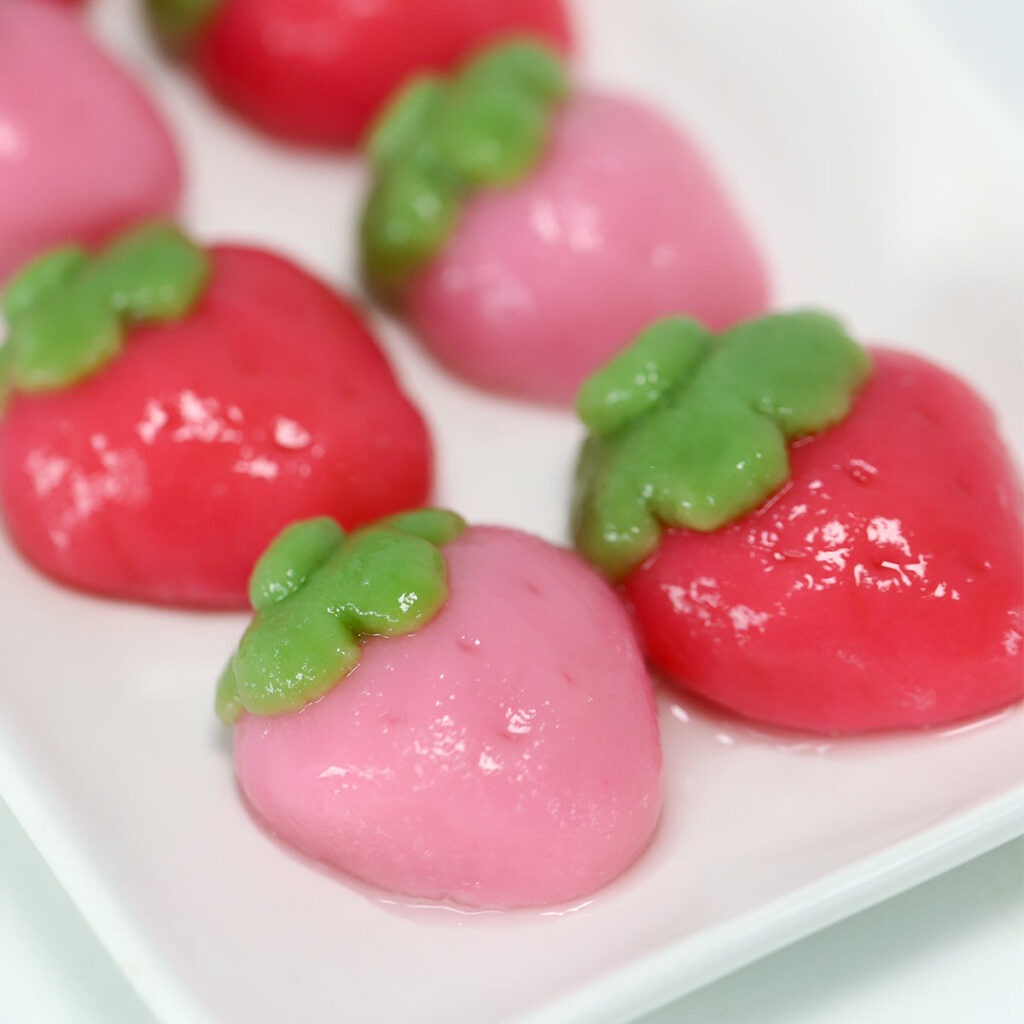 Pink and red strawberry-shaped mochi are on a white rectangular plate.