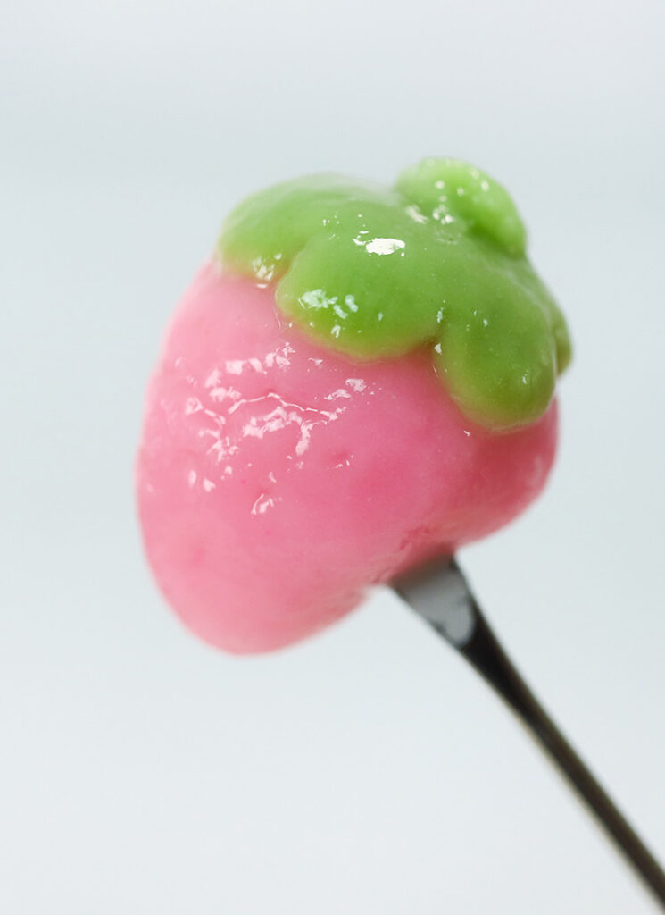 A strawberry-shaped rice cake has been skewered with a food pick.