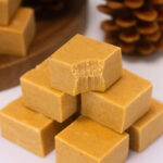 Squares of pumpkin spice fudge are stacked in a pile. A bite has been taken out of the top piece of fudge.