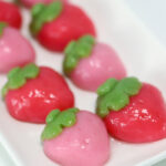Pink and red strawberry-shaped mochi are on a white rectangular plate.