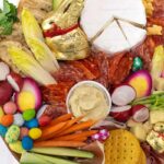 A close up of a charcuterie board of cheese, meat, crackers, vegetables and Easter candy.